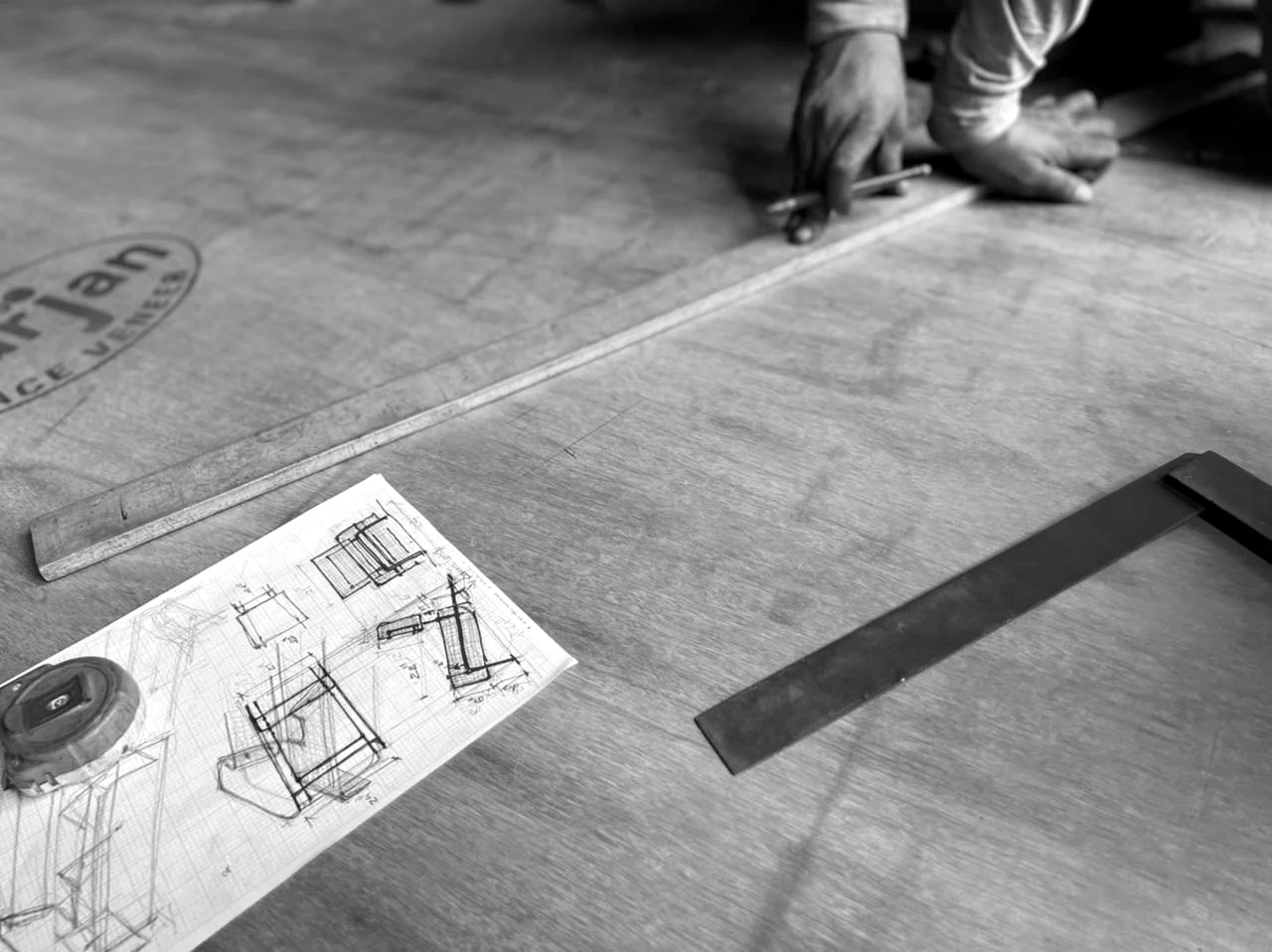 The founder marking timber beside furniture design sketches in the workshop